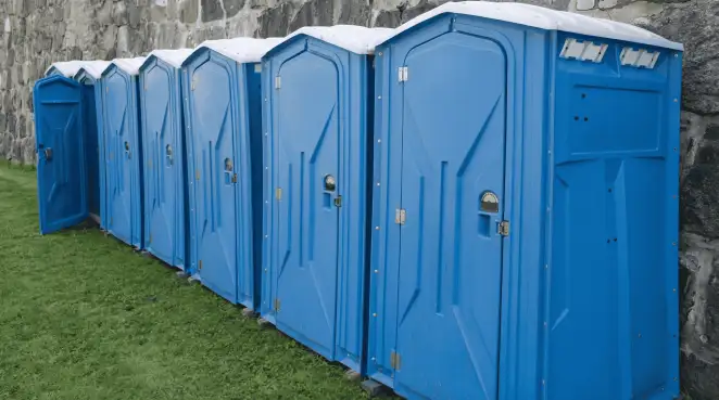 Row of blue portable toilets lined up on grass against a stone wall for event sanitation in Stamford, CT