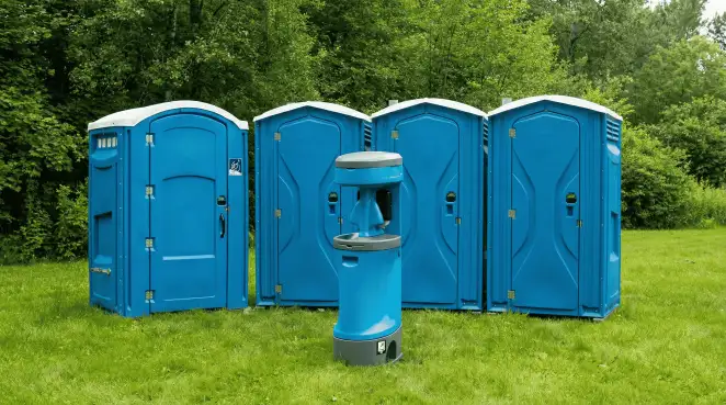 Four blue portable toilets and a matching hand washing station on grass near trees, a common sight at local outdoor events in Stamford, CT