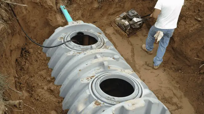 Septic tank installation showing a technician compacting soil around a new poly septic tank in an excavation pit in Stamford, CT